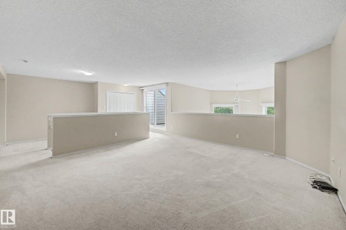 Carpeted open loft area with a partial wall, white sliding doors, and windows providing natural light - #505 7839 96 St Nw, Edmonton, AB 