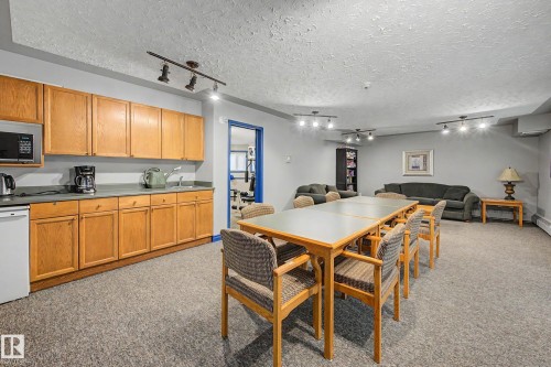 Functional common area featuring ample track lighting, a full wall of wood-finish cabinetry, a utility sink, and durable carpet flooring - #505 7839 96 St Nw, Edmonton, AB 