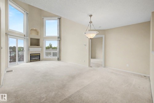 Vaulted ceiling living space featuring an electric fireplace with mantel, built-in wall niches, expansive windows, and a glass sliding door - #505 7839 96 St Nw, Edmonton, AB 