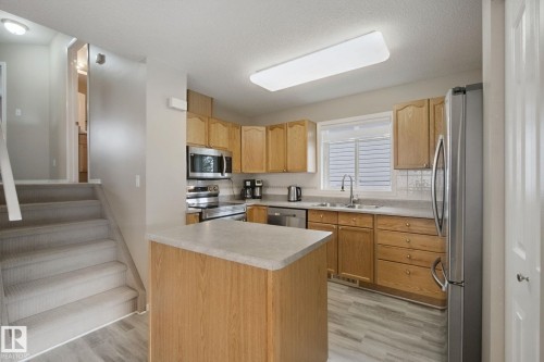 Kitchen featuring wood cabinetry, stainless steel appliances, a center island with a light-toned countertop, and wood-finish flooring - 13912 156 Avenue Nw, Edmonton, AB 