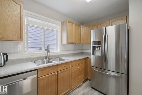 Kitchen featuring wood-finish cabinetry, stainless steel appliances, a double basin sink, and wood-finish flooring - 13912 156 Avenue Nw, Edmonton, AB 