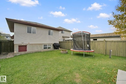 Expansive backyard featuring a manicured lawn, full privacy fencing, a concrete retaining wall, and a side access door - 13912 156 Avenue Nw, Edmonton, AB 