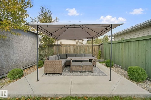 Paved patio area with a covered gazebo structure, bordered by a privacy fence and green shrubbery - 13912 156 Avenue Nw, Edmonton, AB 