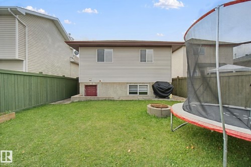 Expansive grassy yard with privacy fencing, a concrete fire pit, and a red-painted exterior basement access door - 13912 156 Avenue Nw, Edmonton, AB 