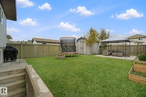 Expansive fenced backyard featuring a concrete patio with a built-in gazebo, a storage shed, and raised garden beds - 13912 156 Avenue Nw, Edmonton, AB 