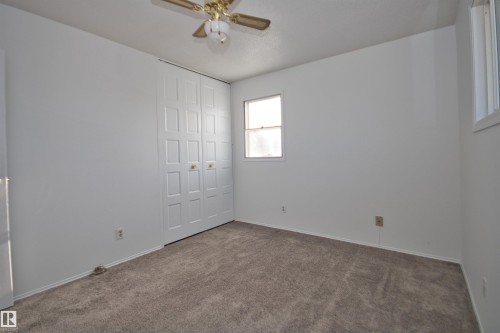 Neutral wall palette, soft carpet flooring, bi-fold closet doors, ceiling fan, and multiple windows - 7743 37 Avenue Nw, Edmonton, AB 