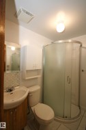 Compact bathroom featuring a curved glass shower enclosure, white wall-mounted storage cabinet, and a pedestal sink with a wood-finish vanity - 