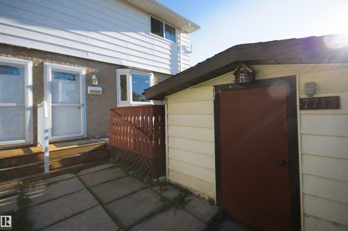 White horizontal siding exterior with a textured stucco lower facade, featuring two entry doors with storm doors, a bay window, and a separate structure with a brown door - 7743 37 Avenue Nw, Edmonton, AB 