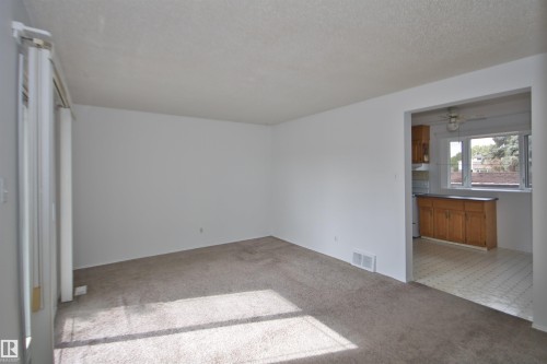 Carpeted flooring, white painted walls, and a doorway leading to a kitchen with wood cabinetry - 7743 37 Avenue Nw, Edmonton, AB 