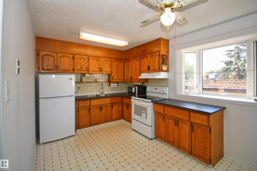 Kitchen featuring wood cabinetry, laminate countertops, a ceiling fan, and a large window - 7743 37 Avenue Nw, Edmonton, AB 