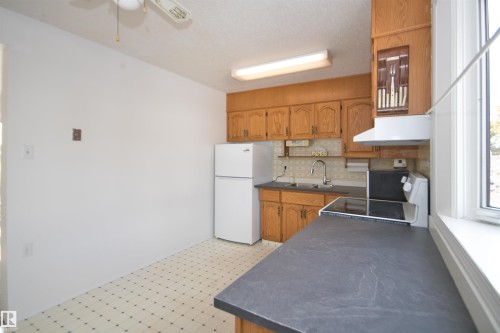Kitchen with wood-finish cabinetry, dark countertops, and patterned vinyl flooring - 7743 37 Avenue Nw, Edmonton, AB 