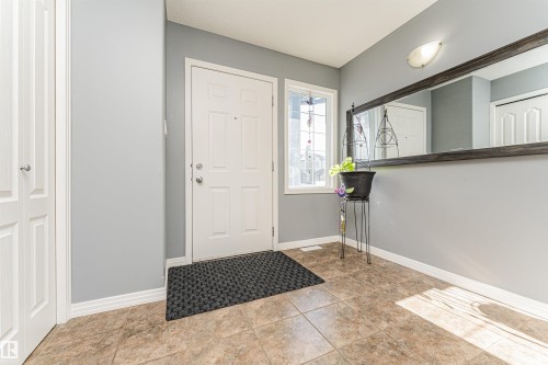 Foyer with tile flooring, a white paneled entry door, a sidelight window, and a built-in closet with bifold doors - 1254 Mcallister Way Sw, Edmonton, AB 