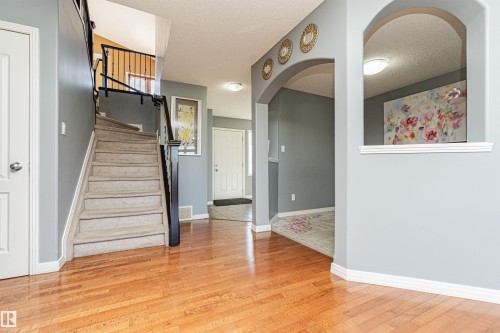 Wood-finish flooring throughout the entry, staircase with carpeted treads and dark wood banister, archway details, and white trim - 1254 Mcallister Way Sw, Edmonton, AB 