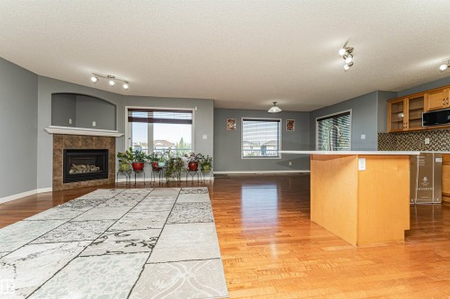 Open-concept living space with wood-finish flooring, a kitchen island with a countertop, and a fireplace with a stone surround - 1254 Mcallister Way Sw, Edmonton, AB 