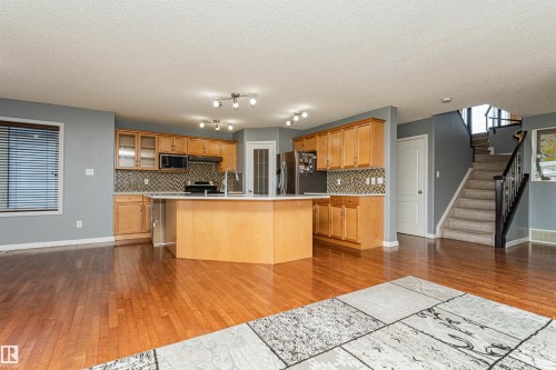 Hardwood flooring, light wood-finish cabinetry, tile backsplash, built-in kitchen island, and carpeted staircase with dark wood-finish railing - 1254 Mcallister Way Sw, Edmonton, AB 