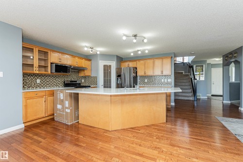 Wood-finish flooring, central island with extended countertop, ample wood cabinetry, tile backsplash, and stainless steel appliances - 1254 Mcallister Way Sw, Edmonton, AB 