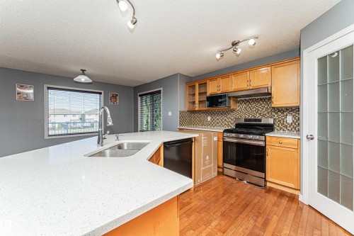 Kitchen featuring wood-finish flooring, light wood cabinetry, stainless steel range, built-in microwave, and a textured tile backsplash - 1254 Mcallister Way Sw, Edmonton, AB 
