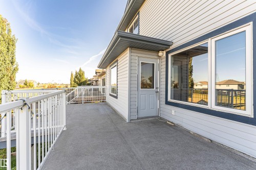 Exterior deck featuring a textured concrete surface, white railing, and direct access to the interior through a glass-paneled door - 1254 Mcallister Way Sw, Edmonton, AB 