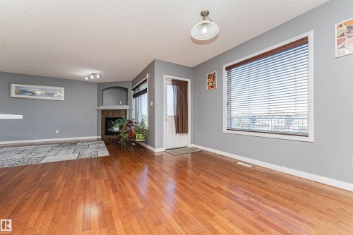 Wood-finish flooring throughout, complemented by a built-in fireplace with a stone surround and mantel, and an arched wall niche - 1254 Mcallister Way Sw, Edmonton, AB 