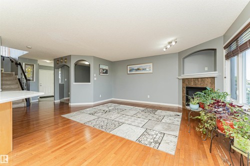 Hardwood flooring throughout, a built-in fireplace with a stone surround, an arched wall niche, and a staircase with an iron railing - 1254 Mcallister Way Sw, Edmonton, AB 