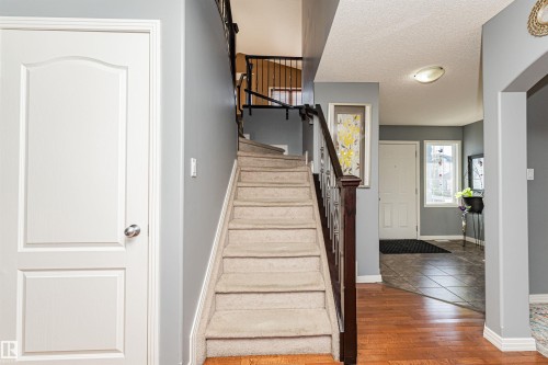 Carpeted staircase with dark wood-finish handrail, tiled entry flooring, wood-finish flooring, and white paneled doors - 1254 Mcallister Way Sw, Edmonton, AB 