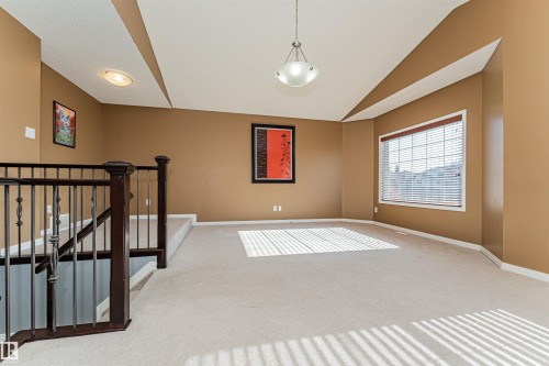 Spacious area with neutral carpeting, a large window, and a decorative pendant light fixture - 1254 Mcallister Way Sw, Edmonton, AB 
