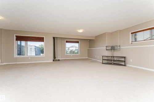 Expansive carpeted area with neutral wall tones and multiple windows, featuring white trim and wood-toned blinds - 1254 Mcallister Way Sw, Edmonton, AB 