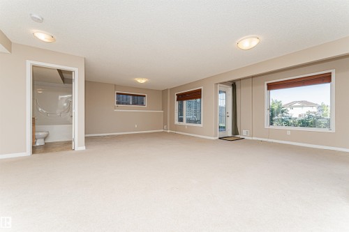 Spacious carpeted room featuring multiple windows, a rear door with a full-light panel, and flush-mount ceiling lighting - 1254 Mcallister Way Sw, Edmonton, AB 