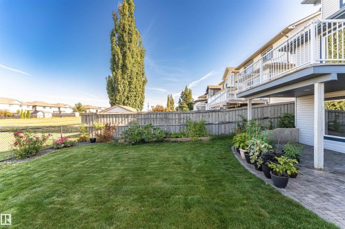 Expansive backyard with a manicured lawn, paver patio, wood privacy fence, and an elevated deck with white railings - 1254 Mcallister Way Sw, Edmonton, AB 