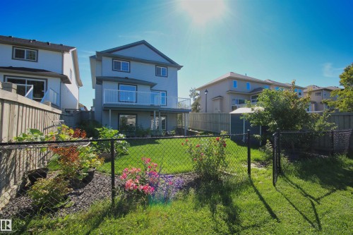 Terraced backyard featuring a chain-link fence, mature plantings, and a manicured lawn - 1254 Mcallister Way Sw, Edmonton, AB 