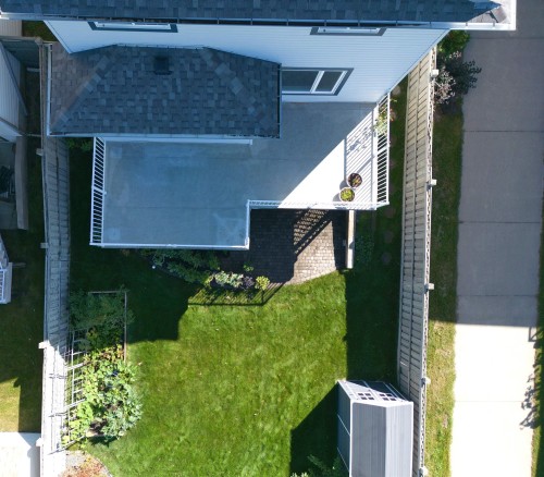 Expansive concrete patio with white railings, a well-maintained lawn, garden beds, and an outdoor storage shed - 1254 Mcallister Way Sw, Edmonton, AB 