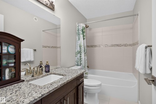 Granite countertop vanity with an undermount sink, brushed nickel faucet, and wood-finish cabinetry - 319 Desrochers Boulevard Sw, Edmonton, AB 