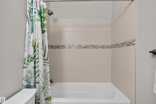 Full-size bathtub with tiled surround featuring an accent tile band and a bronze-finish shower head - 319 Desrochers Boulevard Sw, Edmonton, AB 