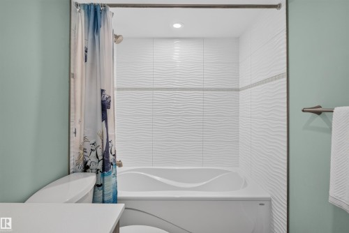 Bathtub with white textured tile surround, decorative accent tile band, recessed lighting, and a brushed nickel towel bar - 319 Desrochers Boulevard Sw, Edmonton, AB 