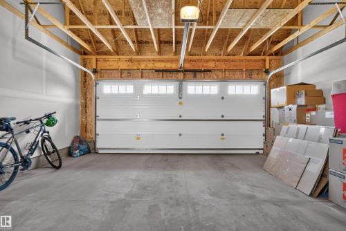 Exposed wood ceiling beams, concrete flooring, overhead garage door opener, and a white paneled garage door with upper window inserts - 319 Desrochers Boulevard Sw, Edmonton, AB 