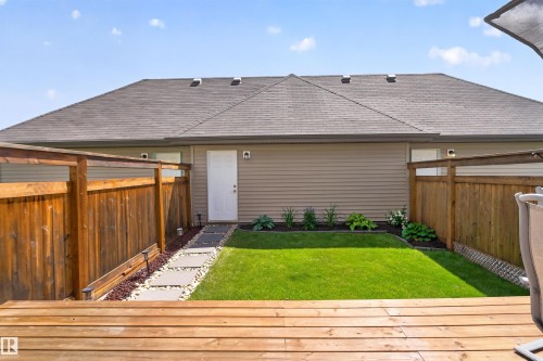 Expansive wooden deck leading to a fenced backyard with a manicured lawn, stone pathway, and landscaped garden beds - 319 Desrochers Boulevard Sw, Edmonton, AB 