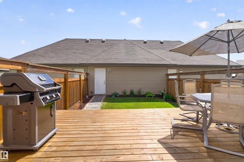 Expansive wood deck with a partial privacy fence, leading to a manicured lawn and garden bed - 319 Desrochers Boulevard Sw, Edmonton, AB 