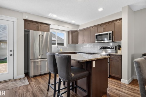 Kitchen with wood-finish flooring, stainless steel appliances, a white subway tile backsplash, and a breakfast bar with stone countertops - 319 Desrochers Boulevard Sw, Edmonton, AB 