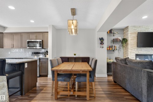 Wood-finish flooring throughout, kitchen with stainless steel appliances, granite countertops, subway tile backsplash, and a stone accent wall with a built-in fireplace - 319 Desrochers Boulevard Sw, Edmonton, AB 
