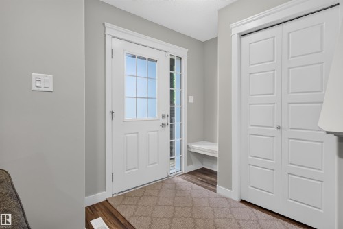 Entryway featuring a white paneled door with glass inserts, wood-finish flooring, a built-in bench, and a paneled closet with bi-fold doors - 319 Desrochers Boulevard Sw, Edmonton, AB 