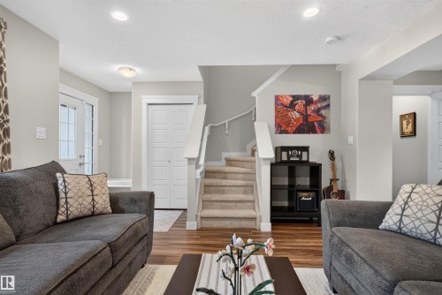 Wood-finish flooring throughout, complemented by a carpeted staircase with white railings - 319 Desrochers Boulevard Sw, Edmonton, AB 