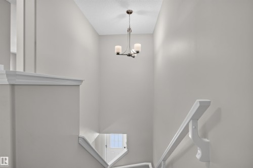 Recessed staircase with white railings, a minimalist chandelier, and light-toned wall finishes - 319 Desrochers Boulevard Sw, Edmonton, AB 