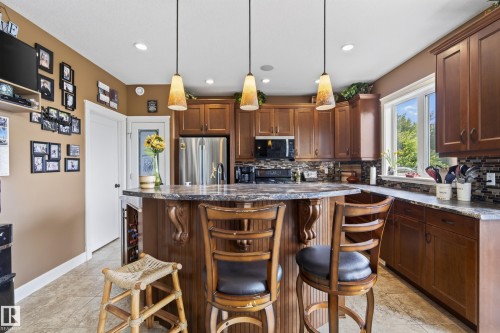 Kitchen featuring wood-finish cabinetry, a central island with a breakfast bar, stainless steel appliances, and a mosaic tile backsplash - 48109 Rr 155, Rural Beaver County, AB - Indoor Photo Showing Kitchen