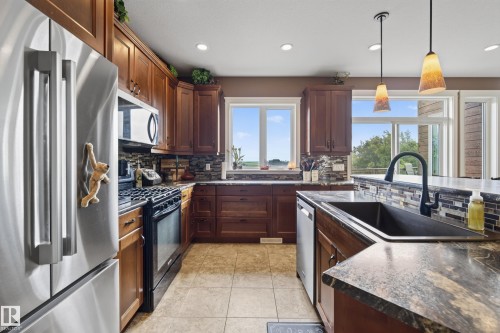 Spacious kitchen featuring stainless steel appliances, rich wood cabinetry, stone countertops, and tile flooring - 48109 Rr 155, Rural Beaver County, AB - Indoor Photo Showing Kitchen With Upgraded Kitchen