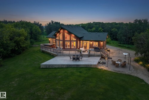 Spacious wood-sided residence featuring a large multi-level deck, expansive lawn, mature tree-lined perimeter, a paver patio with a metal gazebo, and a gravel driveway - 48109 Rr 155, Rural Beaver County, AB - Outdoor With Deck Patio Veranda