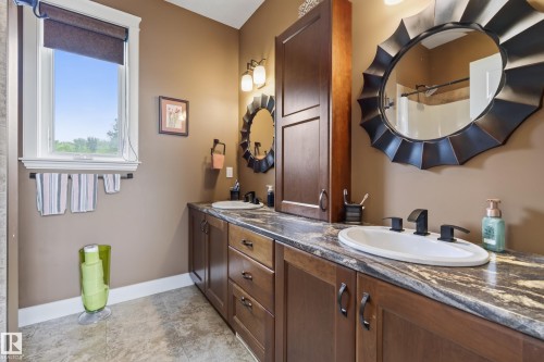 Dual vanity featuring a dark wood-finish cabinet with integrated sinks, dark bronze hardware, and a stone-look countertop - 48109 Rr 155, Rural Beaver County, AB - Indoor Photo Showing Bathroom