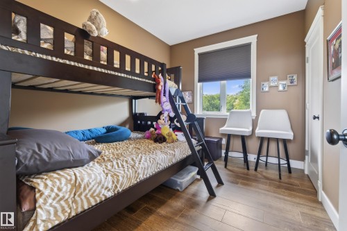 Bedroom featuring a dark wood bunk bed with integrated ladder, wood-finish flooring, a window with a pleated shade, and a white door with black hardware - 48109 Rr 155, Rural Beaver County, AB - Indoor Photo Showing Bedroom