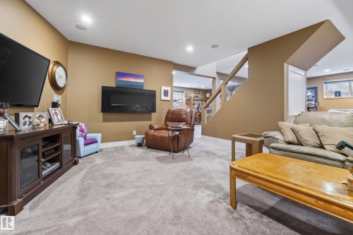 Carpeted entertainment area featuring a wall-mounted fireplace, recessed lighting, and a staircase with a glass railing - 48109 Rr 155, Rural Beaver County, AB - Indoor