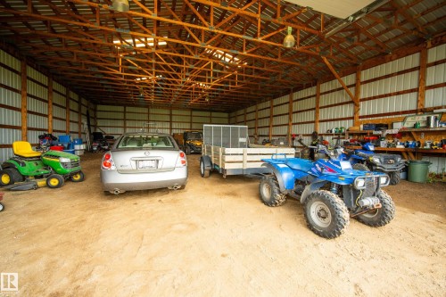 Spacious barn structure featuring a high-pitched roof with exposed wood trusses, corrugated metal siding, and a dirt floor - 48109 Rr 155, Rural Beaver County, AB - Indoor Photo Showing Garage