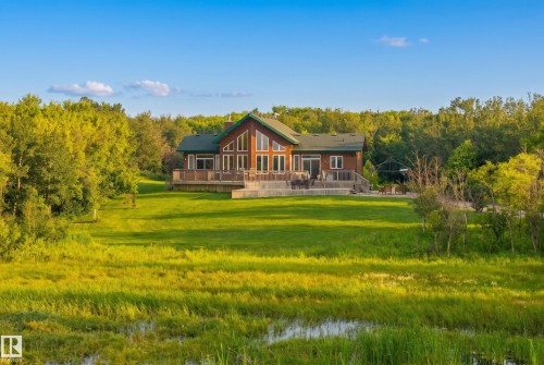 Spacious chalet-style home with expansive windows, a large deck, and a multi-tiered patio, surrounded by mature trees and a natural wetland area - 48109 Rr 155, Rural Beaver County, AB - Outdoor With Deck Patio Veranda